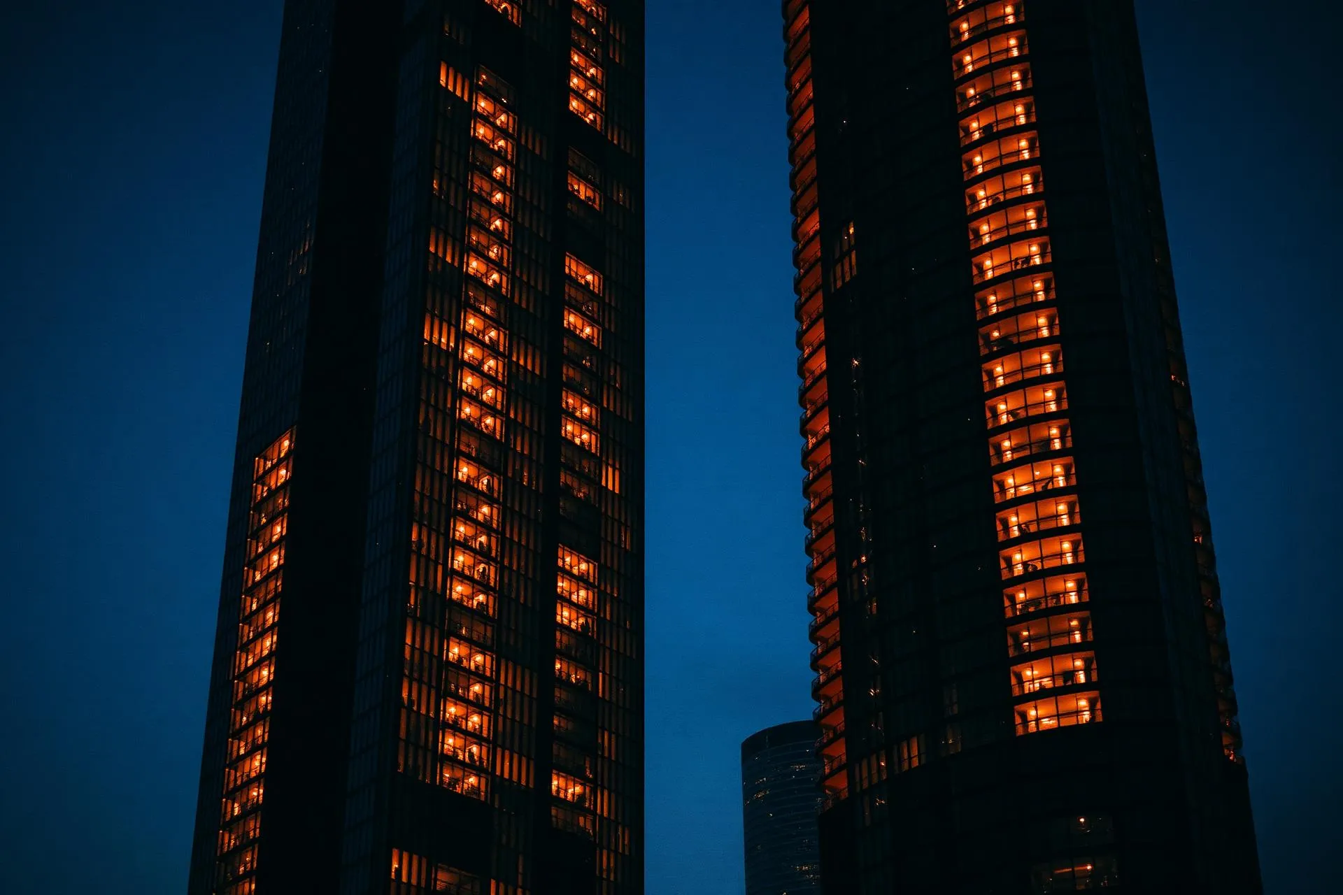 Duas torres residenciais com janelas iluminadas em tom laranja ao anoitecer